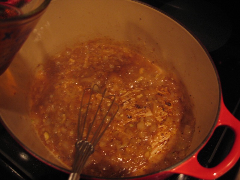 A whisk working sherry into softened onions at the bottom of the pot.