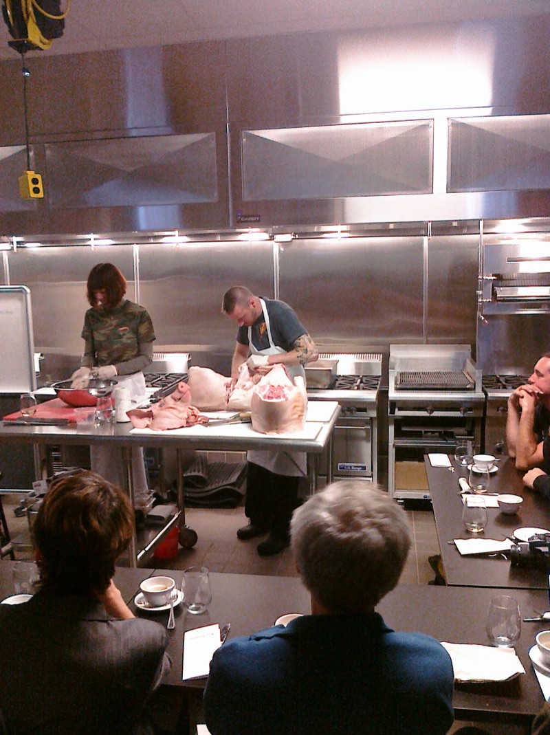 Seen over the shoulders of two guests: butchers at work on the hog at the front of the kitchen.
