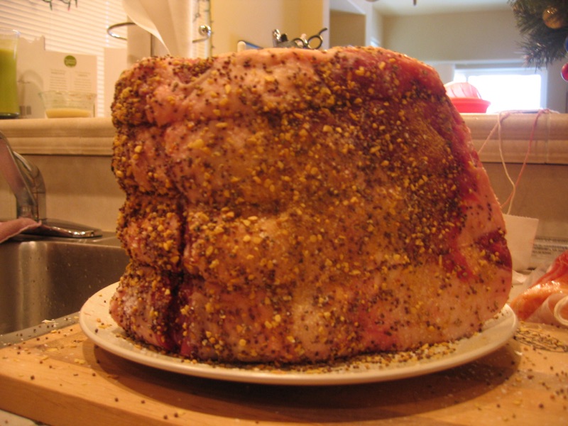 A tall bone-in rib roast crusted with cracked pepper and herbs on a white plate.
