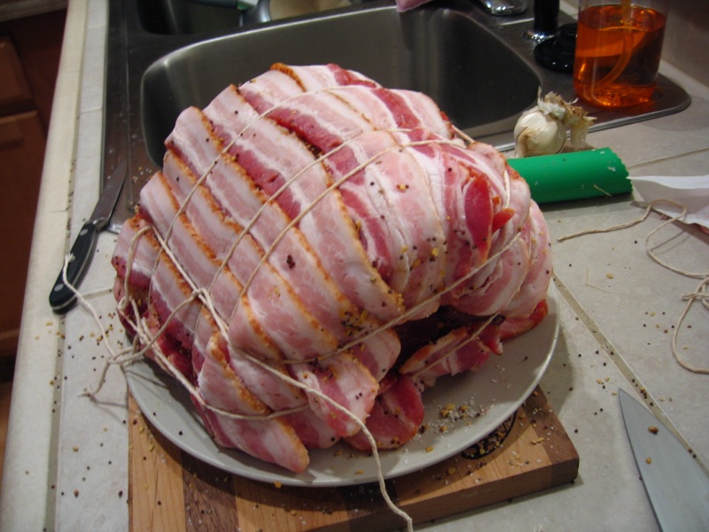 The roast fully wrapped in overlapping bacon strips and tied with butcher's twine.