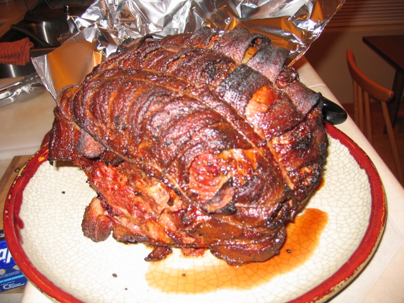 A bacon-wrapped rib roast, dark and lacquered from the fire, resting on a platter.